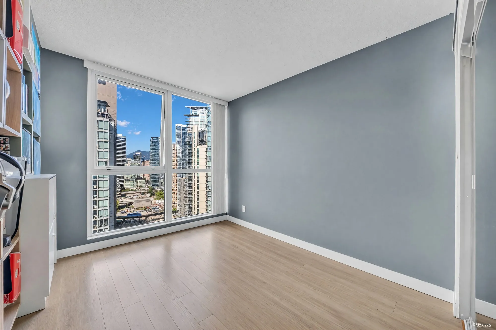 The bedroom shown empty: grey walls, laminate floor, the wall of glass with the towers and the water beyond