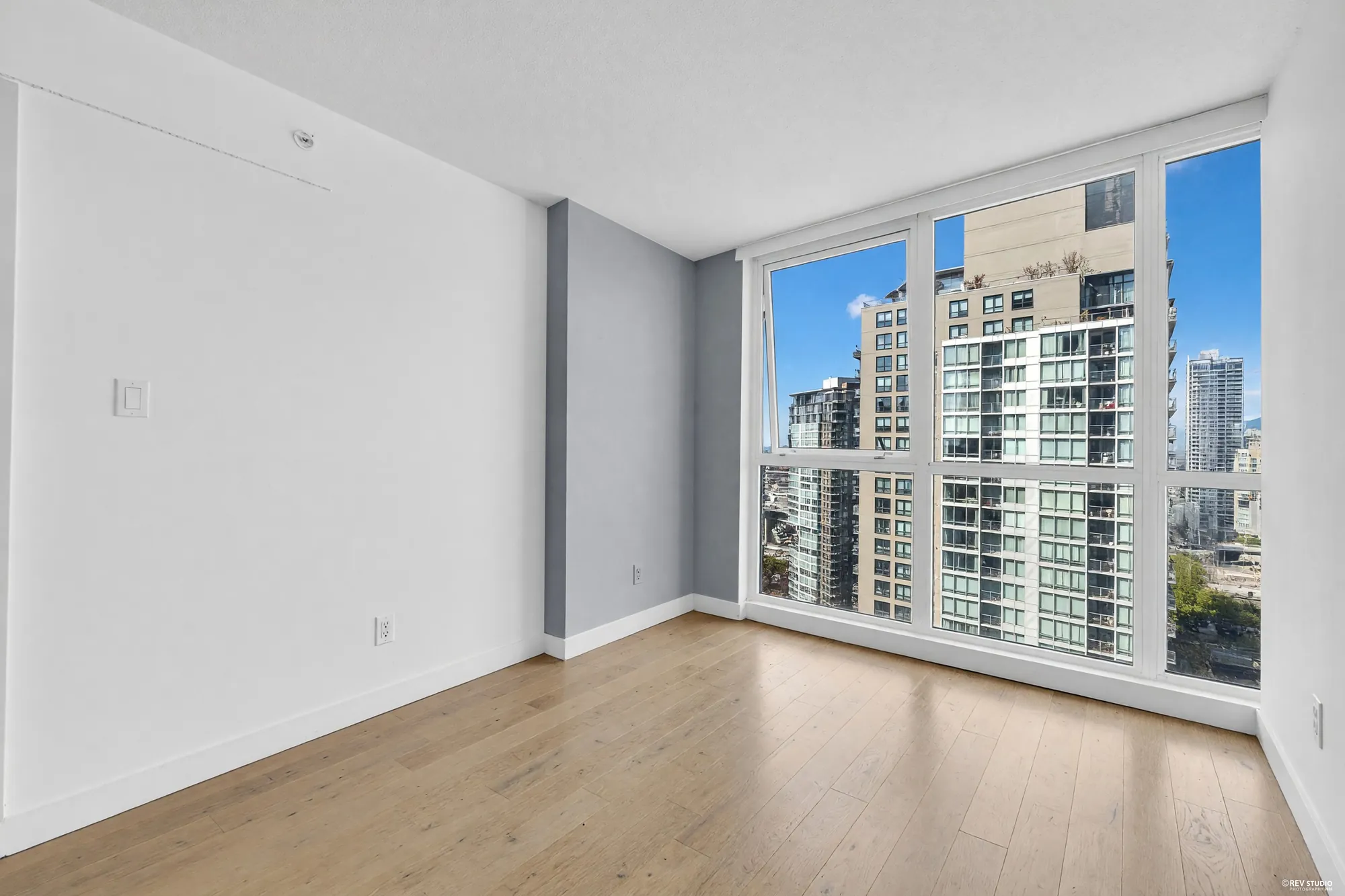 The bedroom from the door, shown empty: the closet wall, the grey accent wall, the glass and the towers beyond