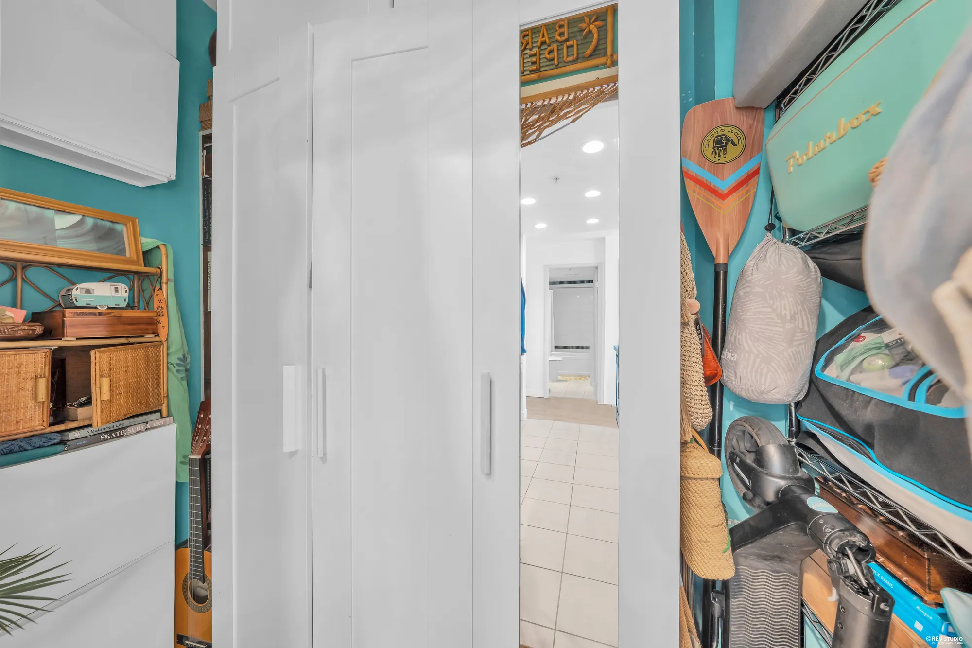 The den off the foyer, used for storage: turquoise walls, a wicker cabinet, a paddle and a bicycle, the hall beyond