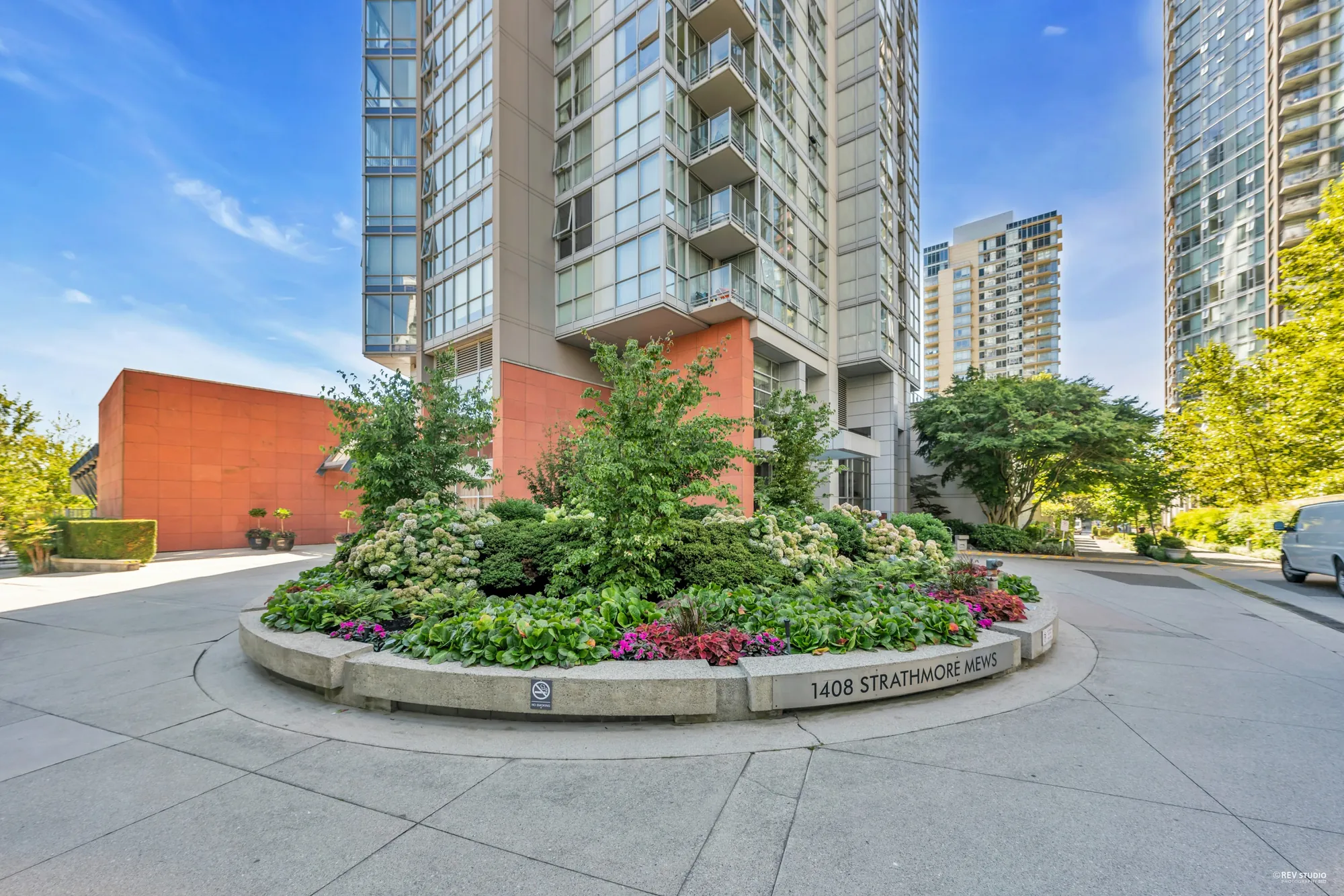 The driveway at the entrance with the 1408 Strathmore Mews sign in a flower bed, the tower above