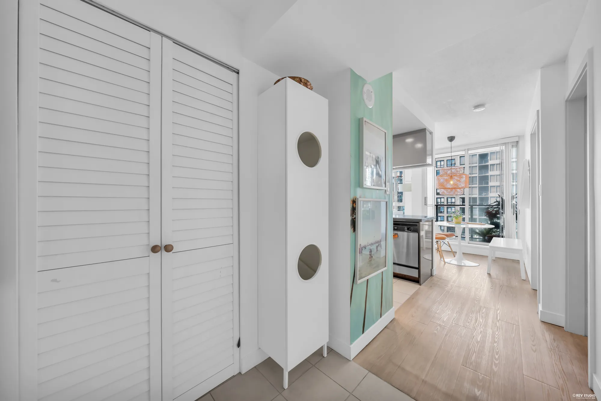 The foyer: louvred closet doors, a tall white cabinet, the kitchen and the window beyond