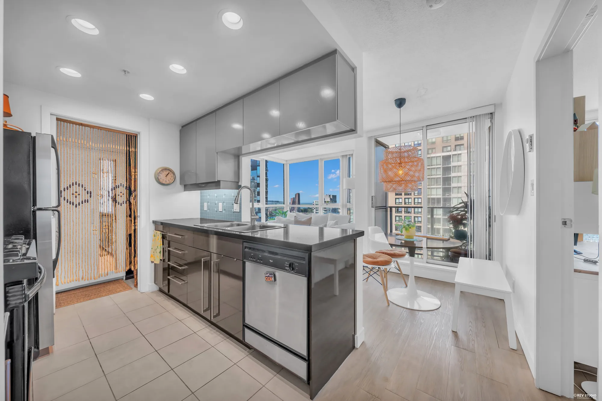 The galley kitchen from the door: black granite counters, a stainless fridge and dishwasher, the dining table and the view at the end