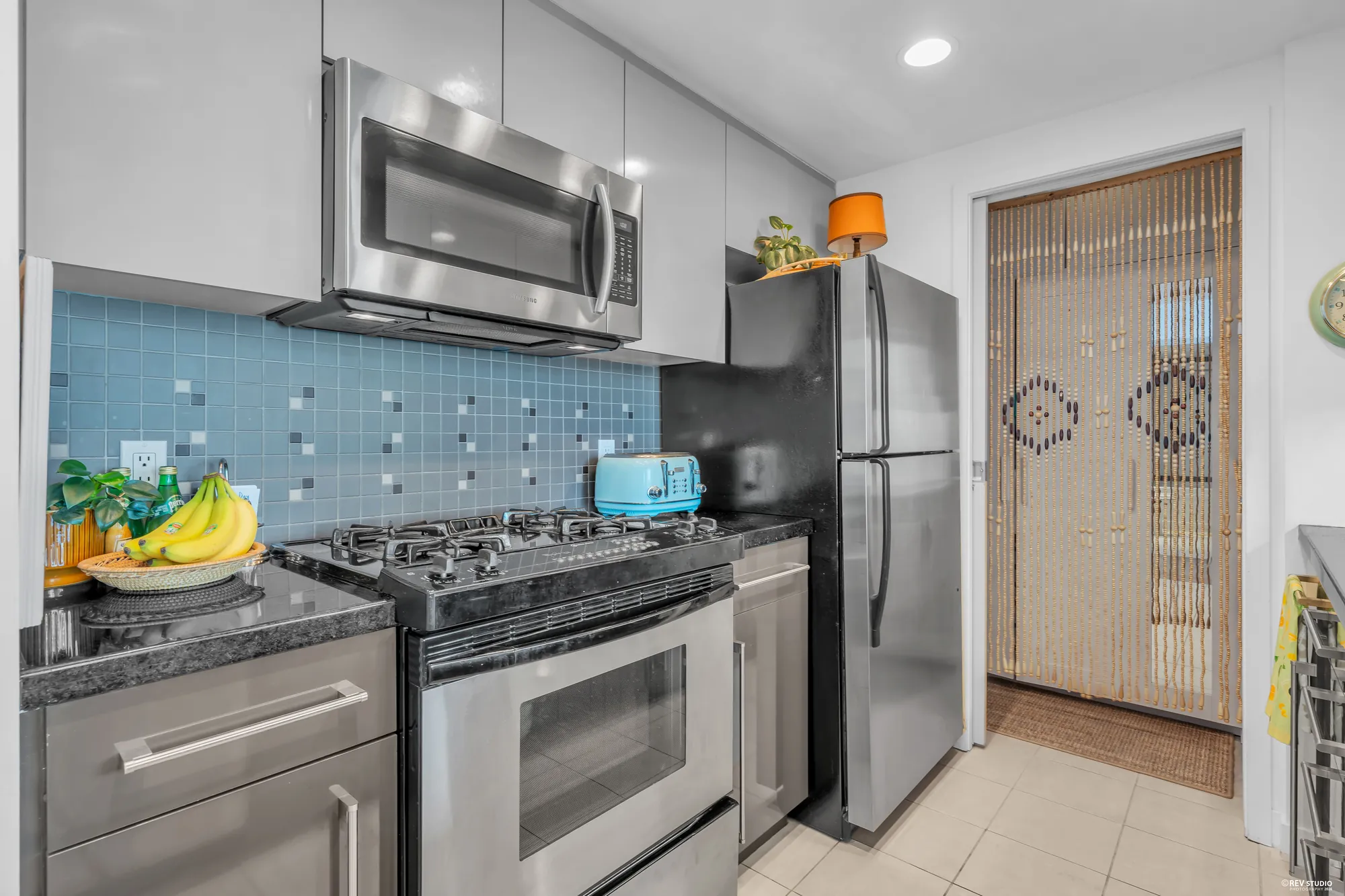 The range and the stainless fridge, the blue tile backsplash, a beaded curtain in the doorway