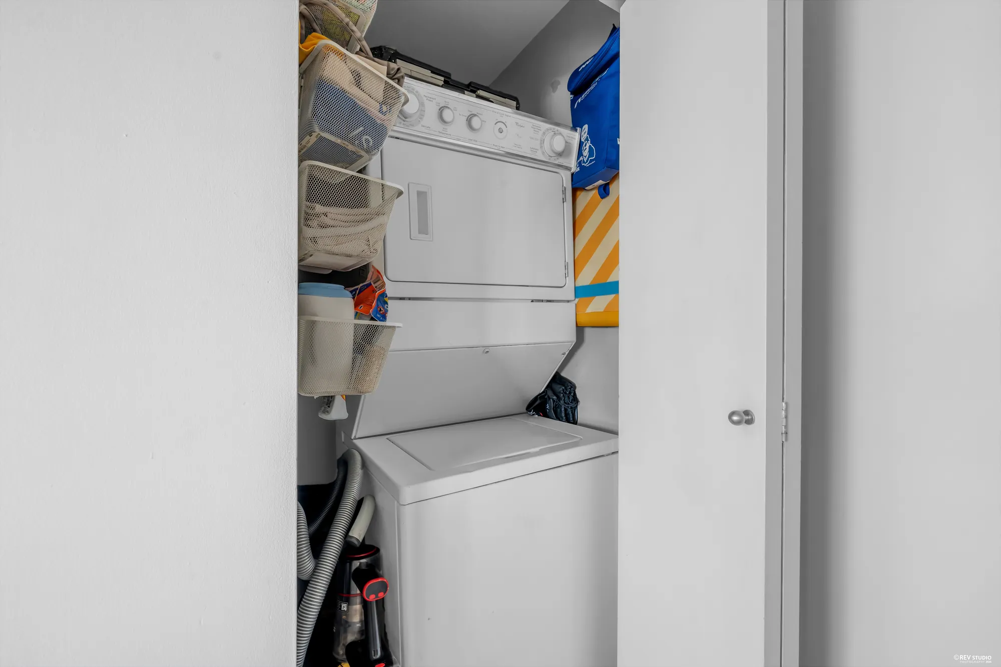 The laundry closet with a stacked washer and dryer and shelves above
